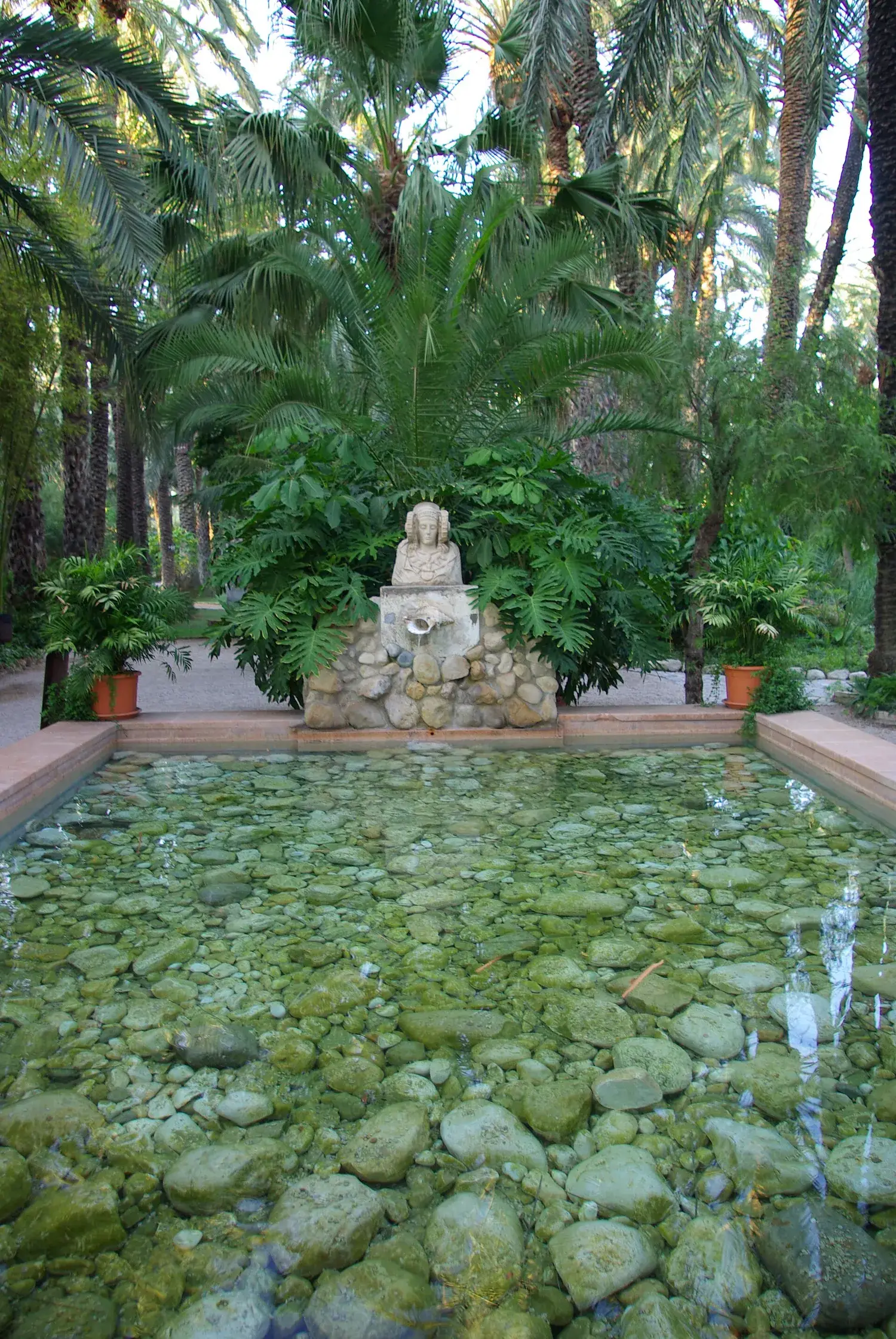 Vijver en fontein omringd door palmen in de tuin Huerto del Cura