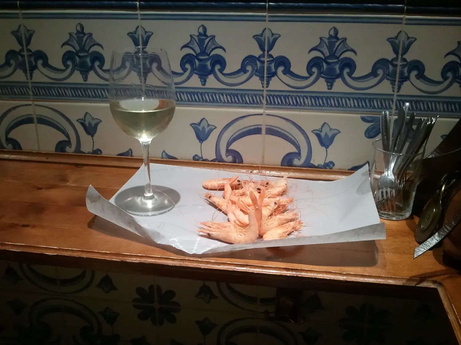 Tapa de gambas blancas con una copa de vino blanco sobre una barra de azulejos