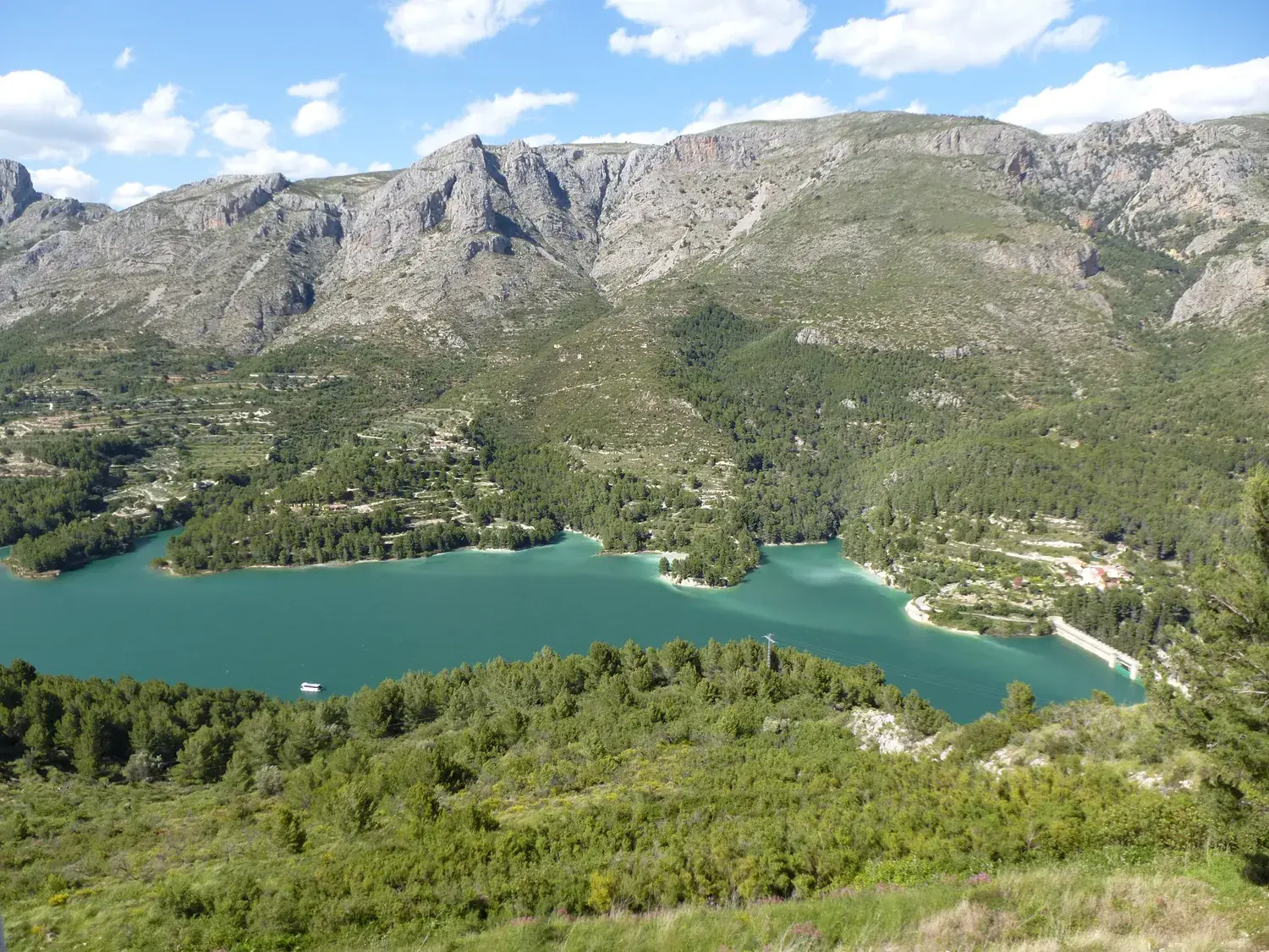 The turquoise Guadalest reservoir surrounded by mountains and pine forest