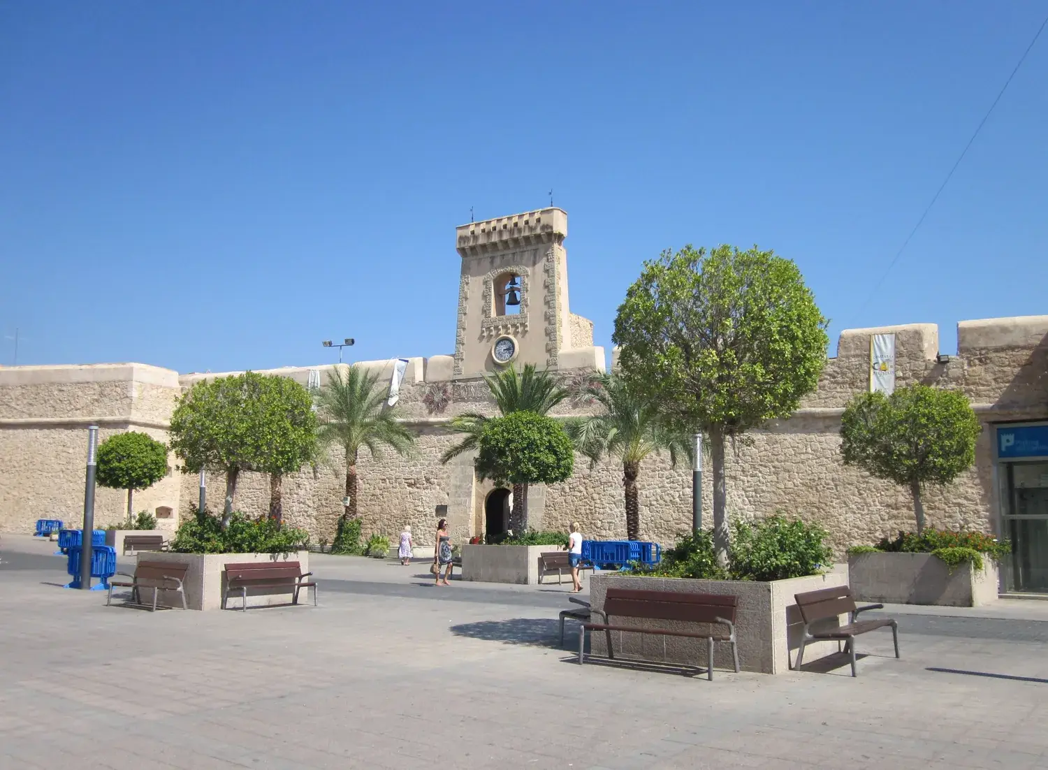 Santa Pola fortress, with its stone walls and tower, on a tree-lined square