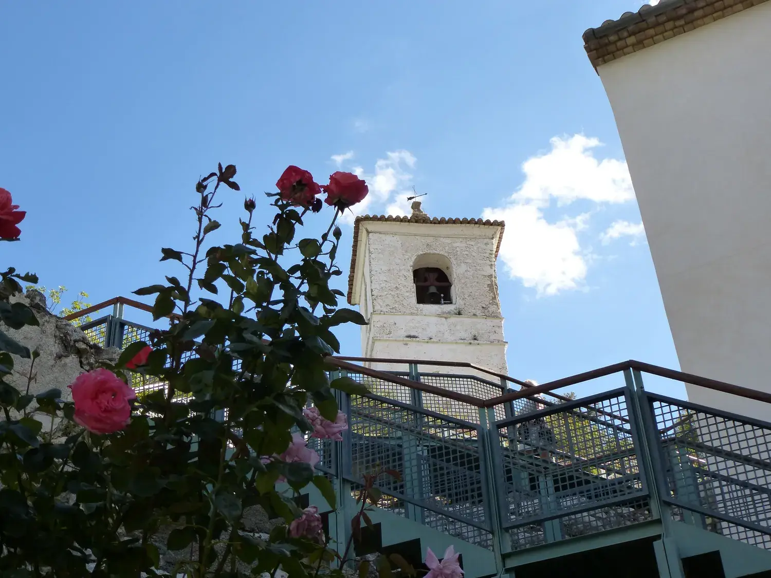 Guadalest’s bell tower seen from a terrace with blooming roses