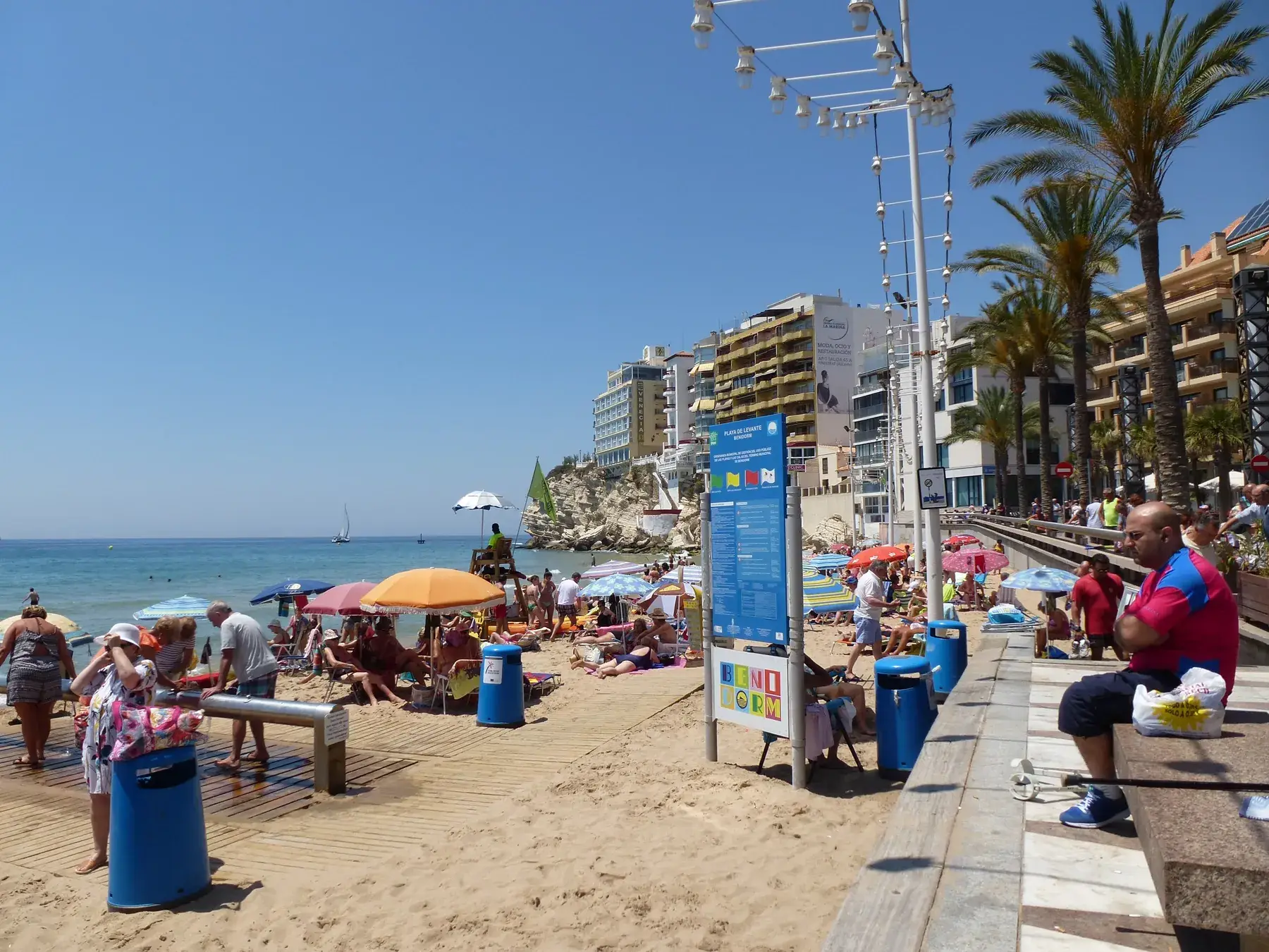 Families strolling along Levante beach in Benidorm, parasols and blue sea