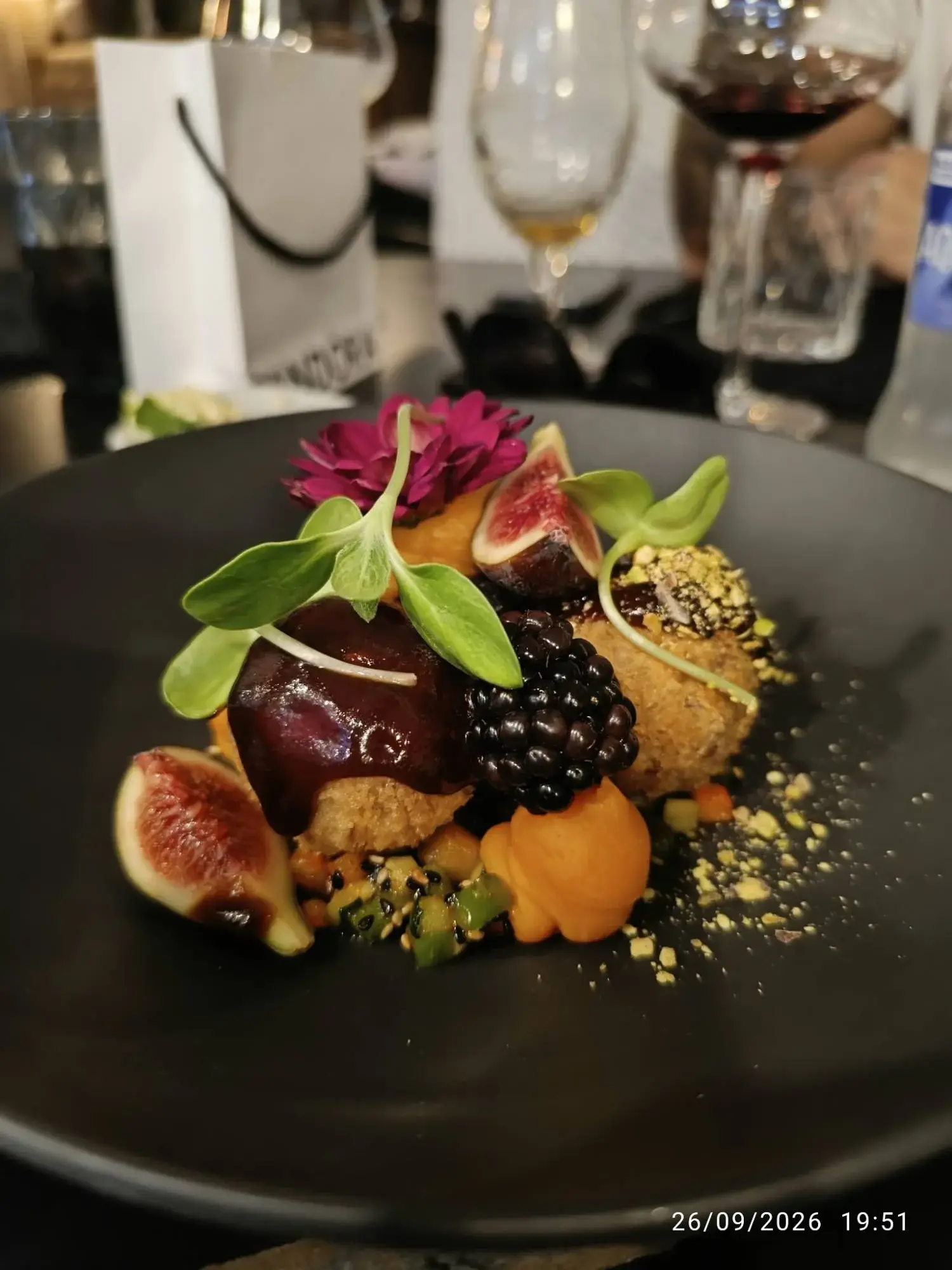 Croquetas van gekonfijte eend bij Restaurante Luka op een zwart bord, met vijgen, braambes, oranje puree, donkere saus, gehakte pistache, scheuten en een paarse bloem
