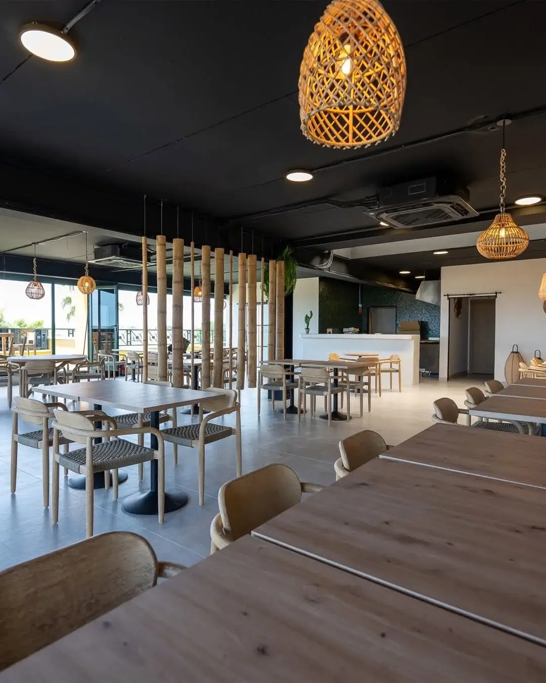Lichte eetzaal van Hola Patatas met houten tafels, gevlochten stoelen, rotan hanglampen en een bamboe scheidingswand