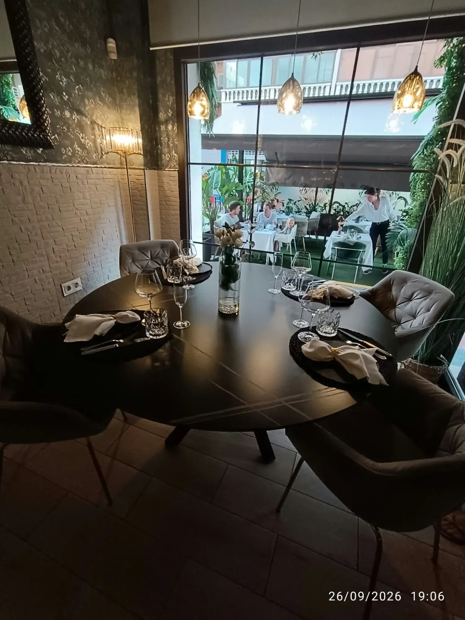 Gedekte ronde tafel binnen in Restaurante Luka, met wijnglazen en geknoopte servetten, en door het grote raam zicht op het groene terras