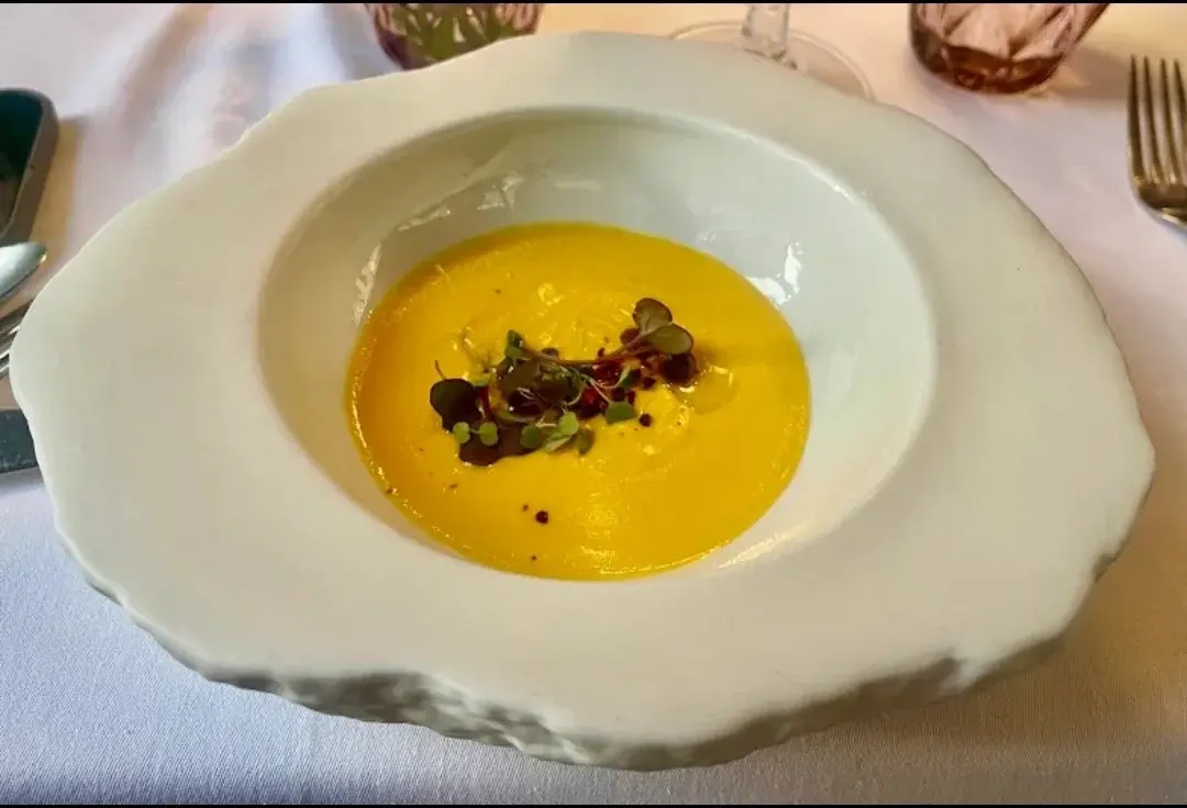Aangeboden pompoenvelouté bij Restaurante Luka, geserveerd in een wit diep bord met onregelmatige rand en afgewerkt met scheuten